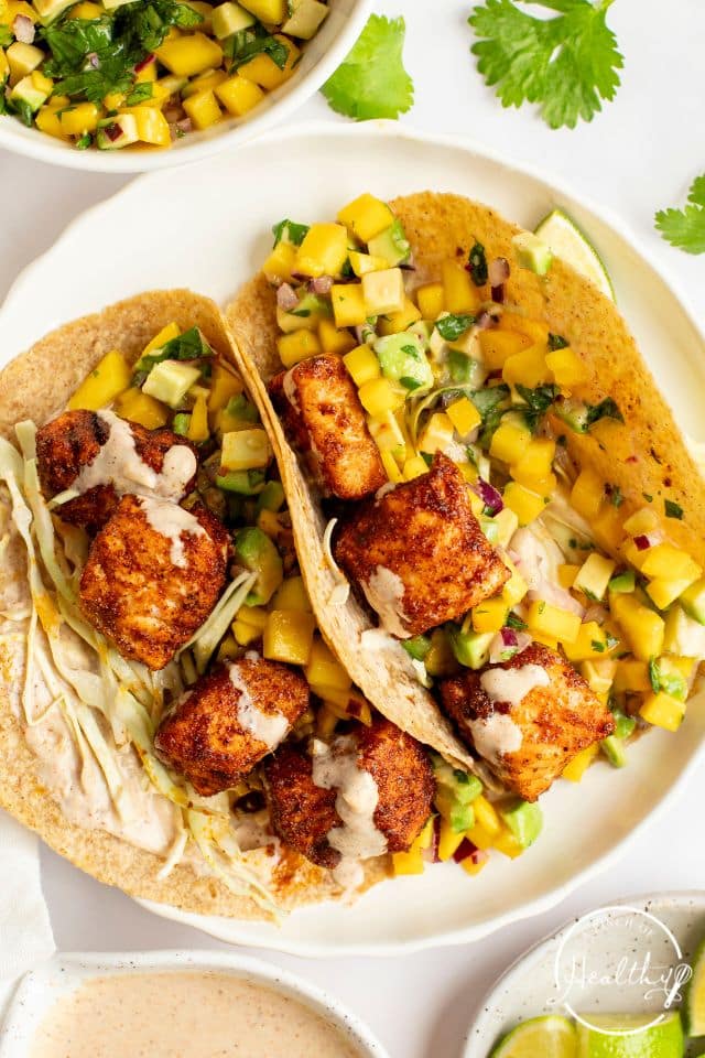 Salmon tacos on a white plate with cilantro and salsa on top.
