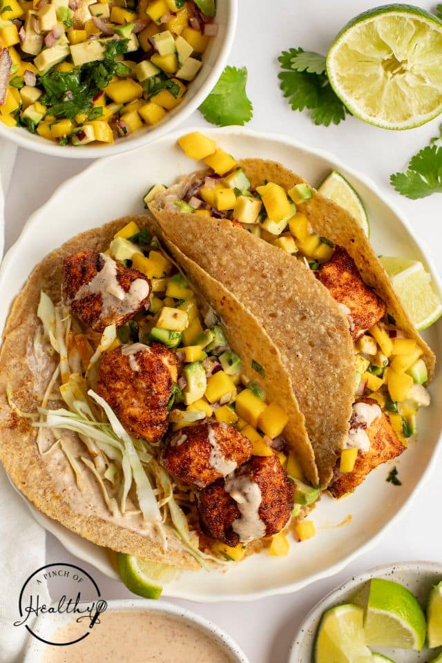 Finished salmon tacos on a white plate with limes. 