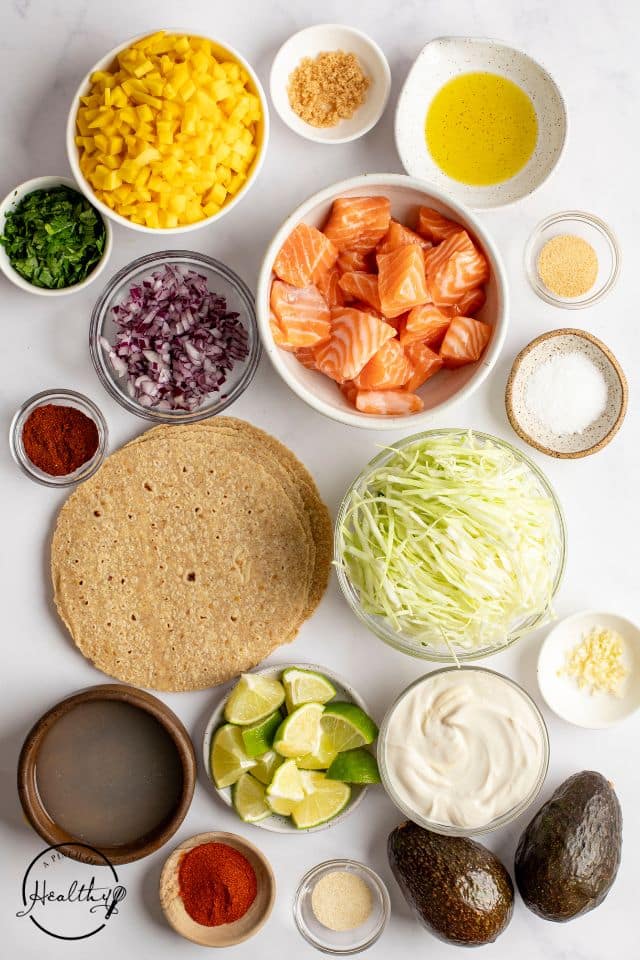 Ingredients for salmon tacos on a white background in separate containers.