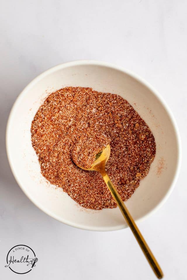 Seasoning for salmon tacos in a white bowl with a gold spoon.