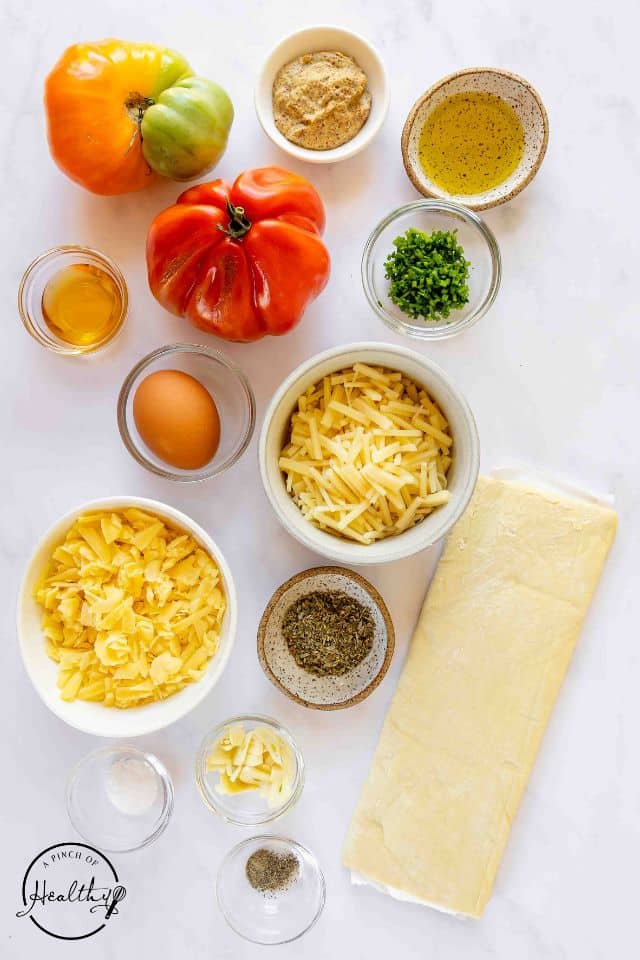 Ingredients for tomato tart in separate containers on a white background.