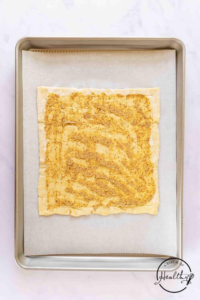 Dijon mustard spread over the top of the puff pastry sheet.