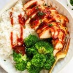 Baked Barbecue Chicken Breast with rice and broccoli and BBQ sauce drizzled on top.