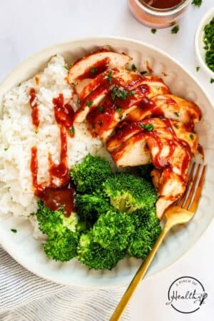 Baked Barbecue Chicken Breast with rice and broccoli and BBQ sauce drizzled on top.