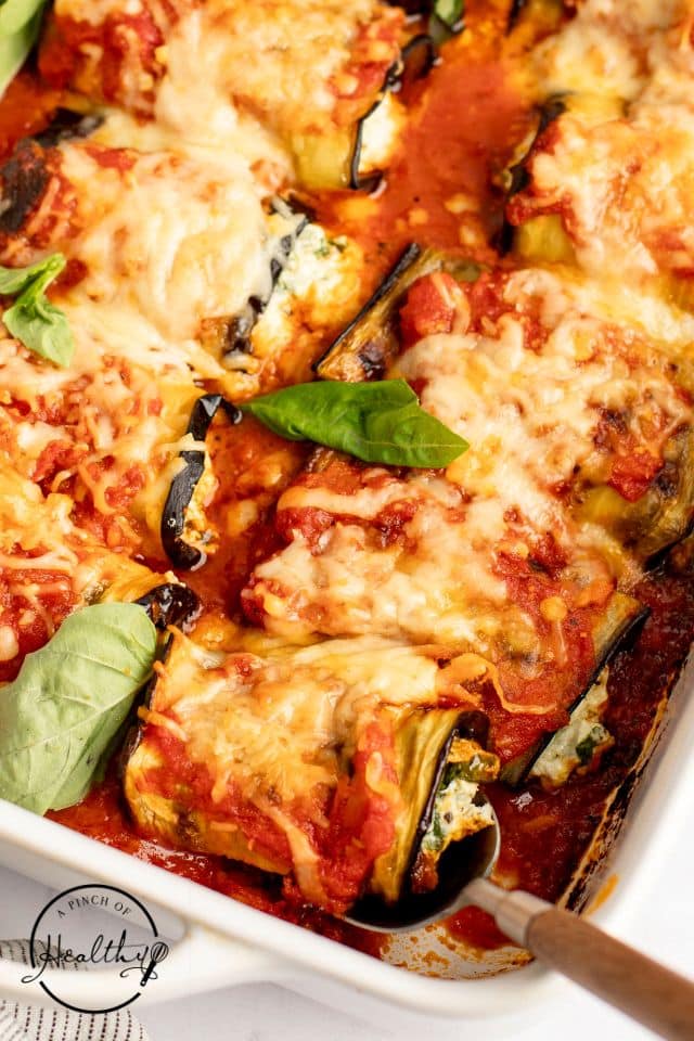 Dish of eggplant rollatini with fresh basil on top in a white casserole dish.
