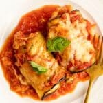 Two eggplant rollatini portions on a white plate with a gold fork.