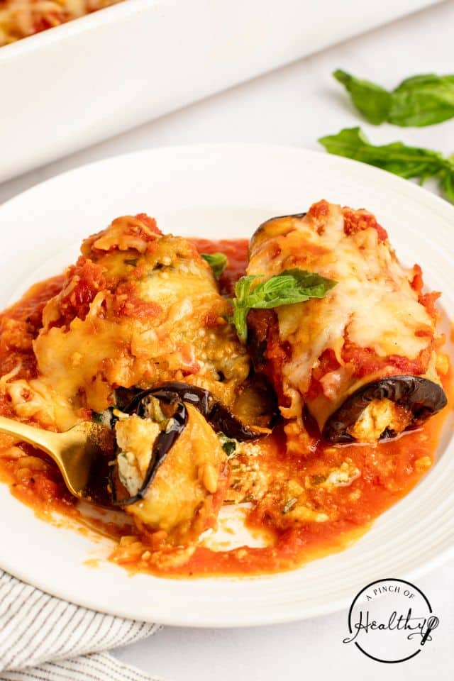 Two eggplant rollatini on a white plate with a gold fork.