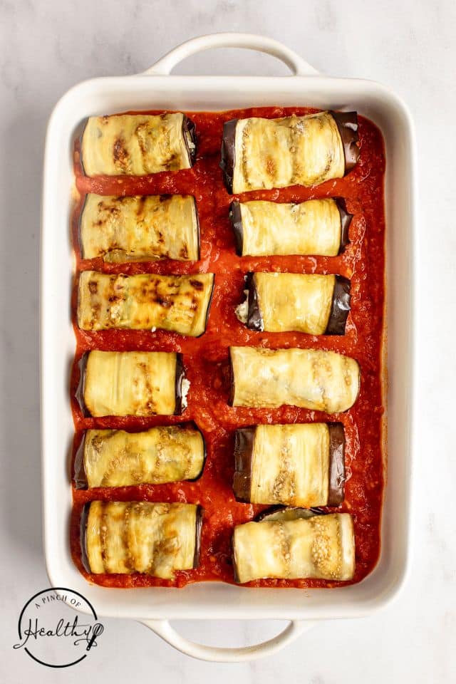 Rolled up stuffed eggplant in a baking dish with marinara on the bottom.