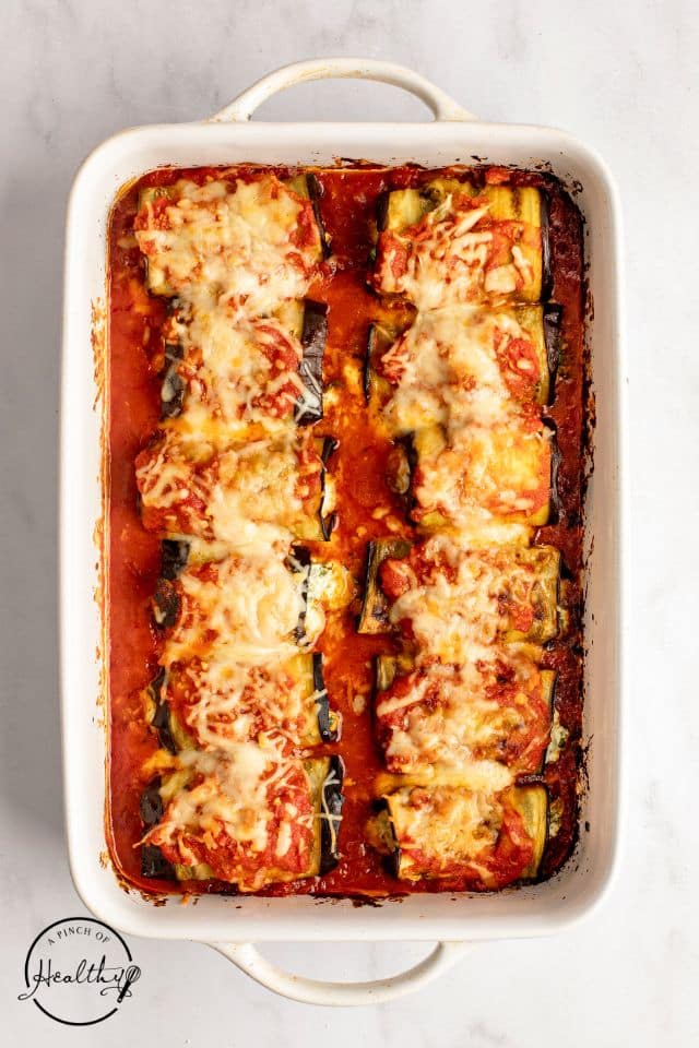 Baked eggplant rollatini in a large rectangular baking dish with melted cheese on top.