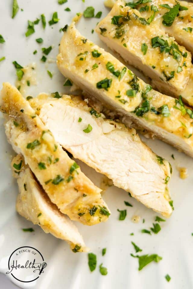 Sliced breasts of garlic butter chicken on a white plate.