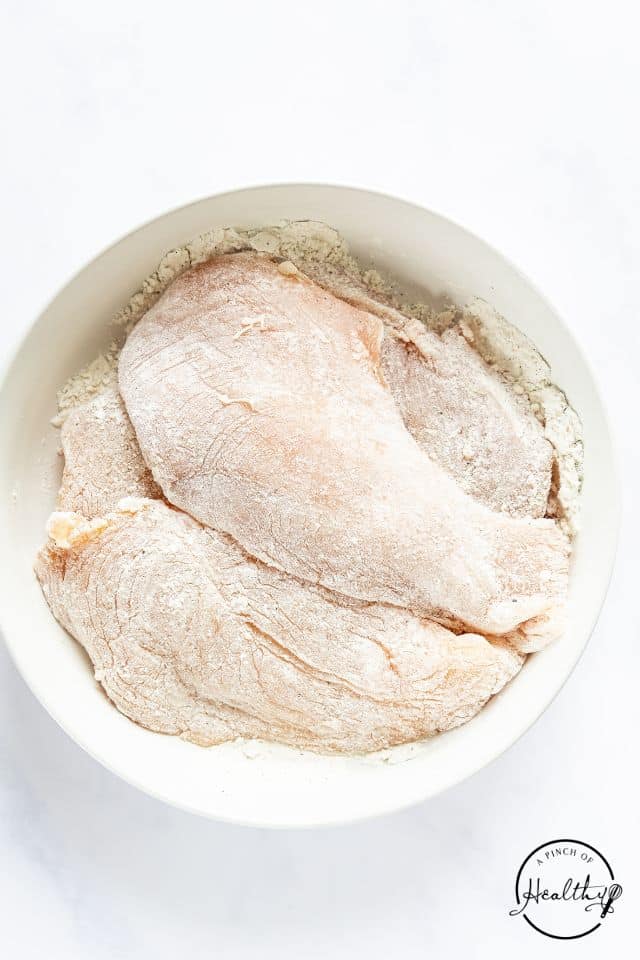 Chicken breasts seasoned and dredged in flour in a large white bowl.