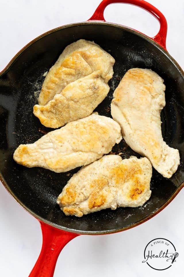 Browned chicken breasts in a large skillet on a white background.