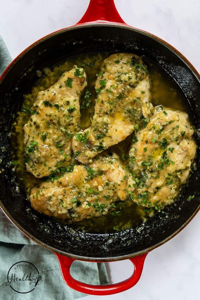 A large skillet with cooked chicken drenched in garlic butter sauce.