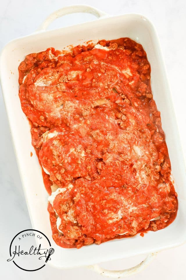 A layer of meat sauce over the top of the cheese and pasta in a large rectangular baking dish for lasagna.