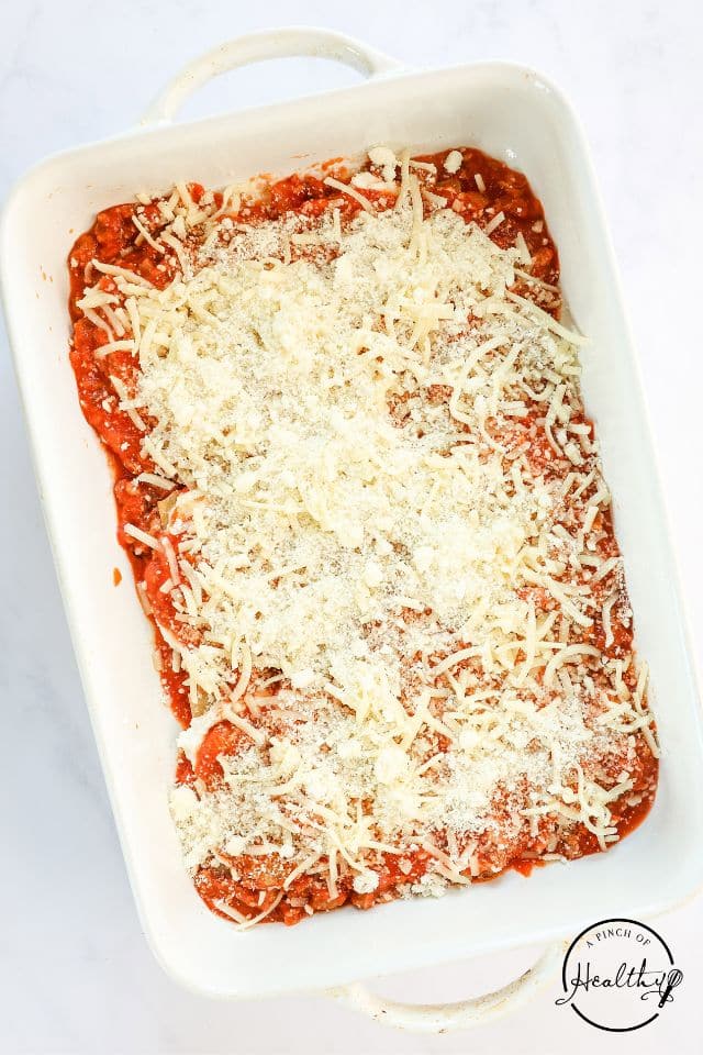 Homemade lasagna being layered into a large white rectangular baking dish.