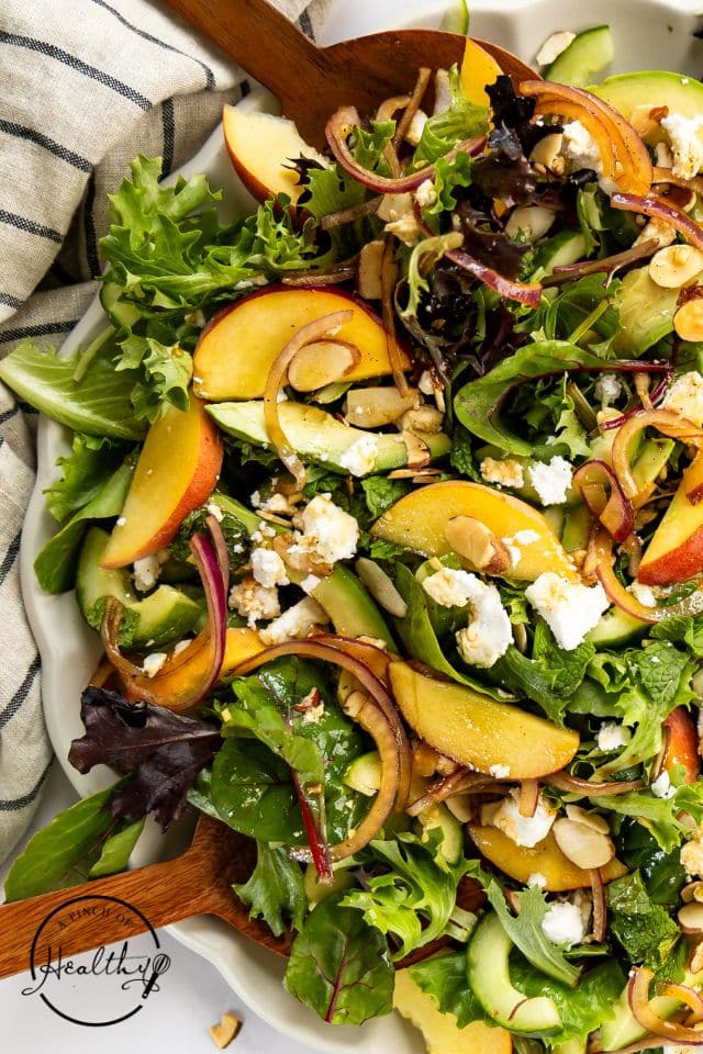 Completed peach salad in a large serving bowl with a wooden spoon inside.
