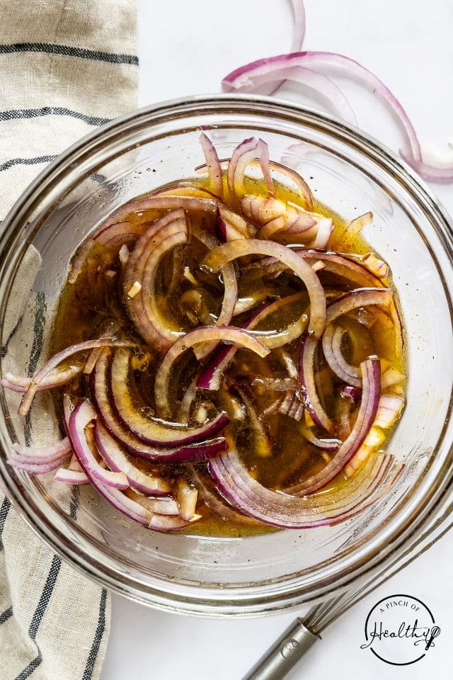 Onions marinating in the dressing in a glass bowl.