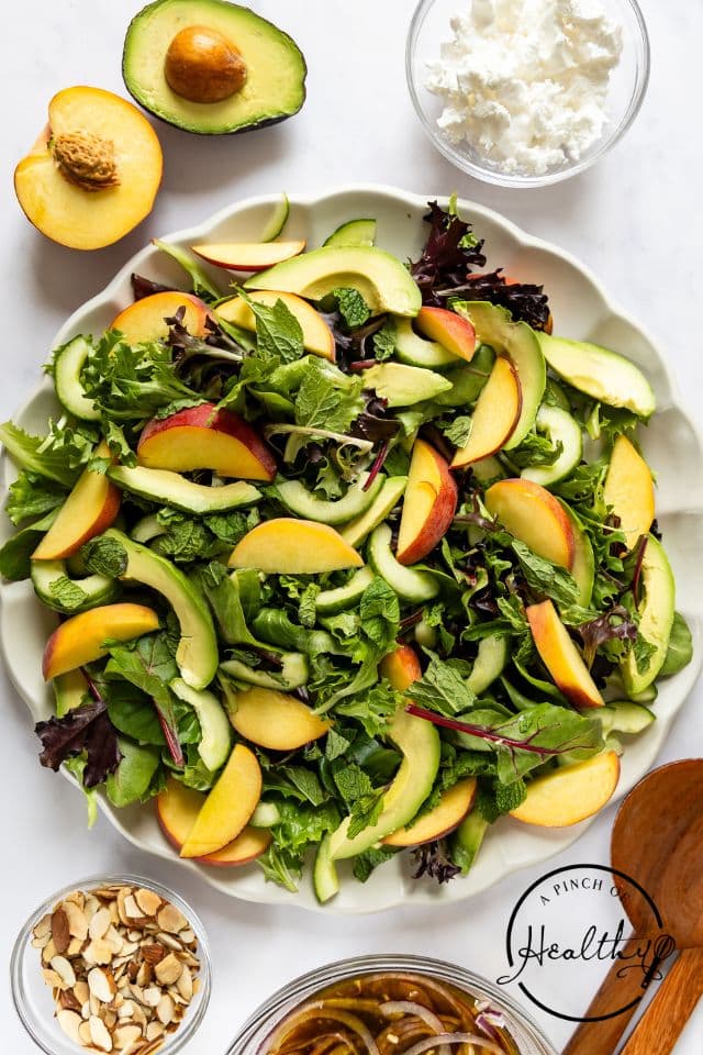 Greens, peaches, avocado, and cucumber in a large serving bowl.