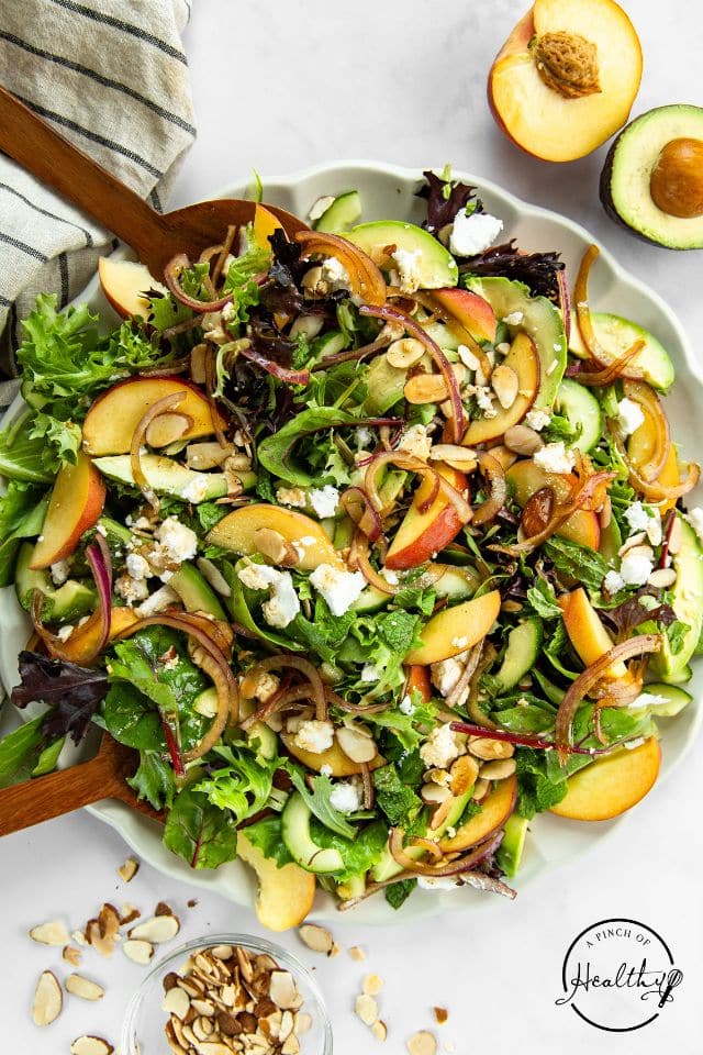 Peach salad in a large serving bowl with a halved avocado near the bowl.