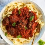 Meatballs with red sauce on a plate of pasta.