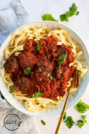 Meatballs with red sauce on a plate of pasta.