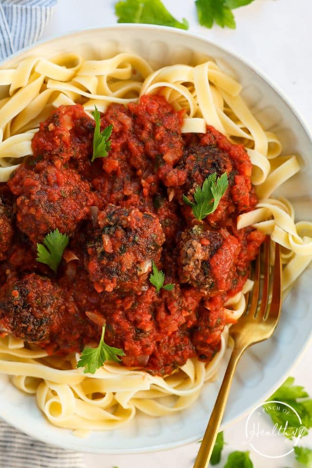 Homemade meatballs and pasta on a large platter with parsley on top.