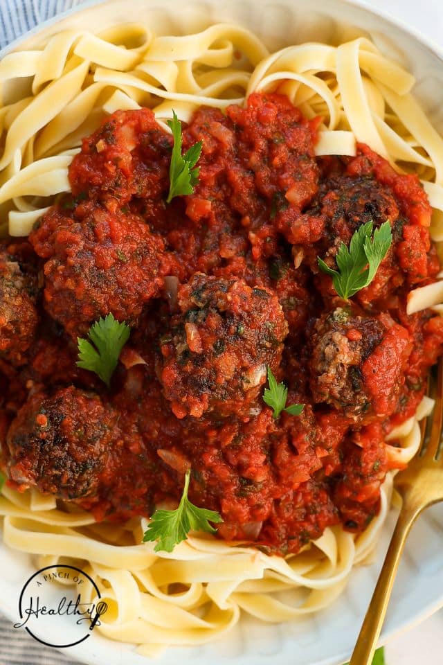 Homemade meatballs on a plate of pasta with parsley on top.