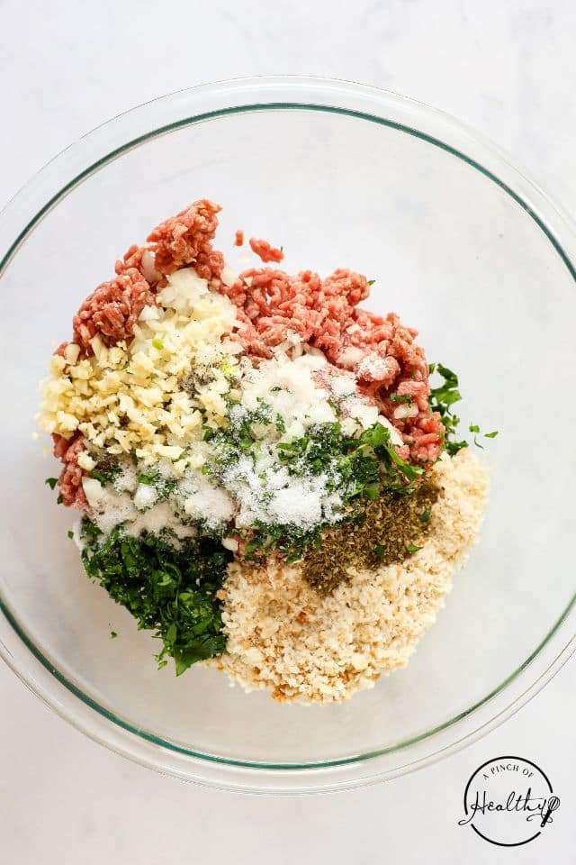 Ingredients for meatballs in a large glass bowl. 