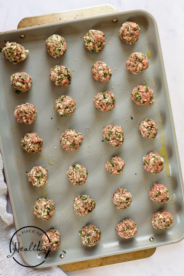 Meatballs placed on a prepped cookie sheet after being formed into balls.