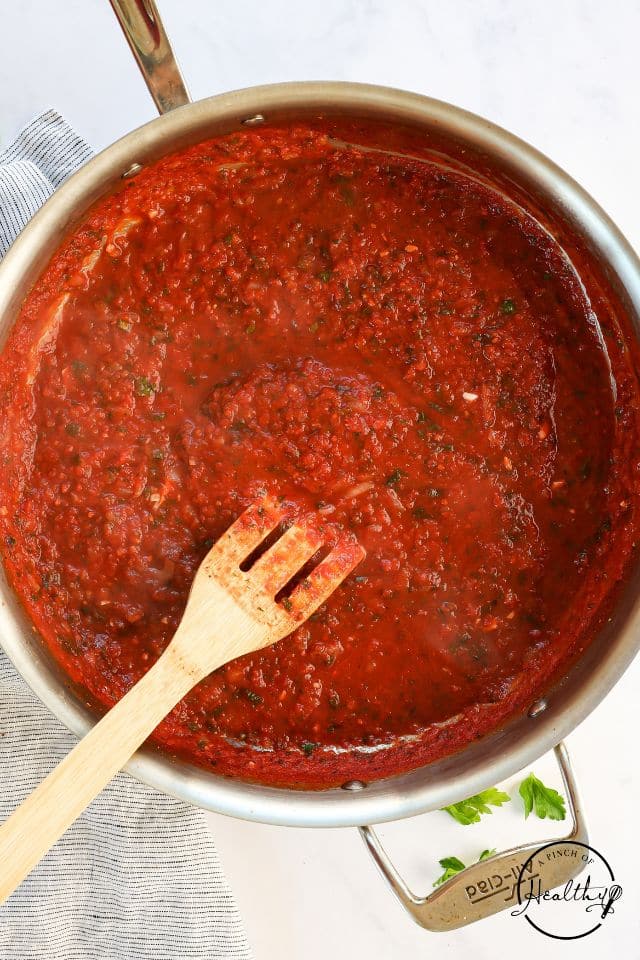 Red sauce in a large skillet with a wooden spoon inside.