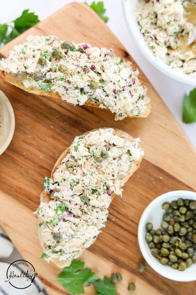 Salmon Salad on toast with capers in a dish to the side.