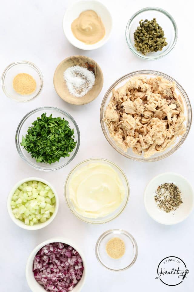 Ingredients for salmon salad in separate containers on a white background.