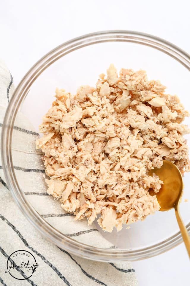 Salmon after being drained and chunked apart in a glass bowl. 