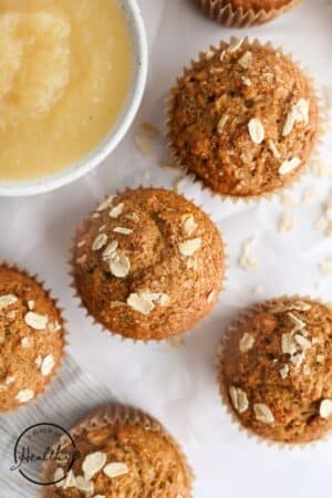 Applesauce muffins with oats on top and a bowl of applesauce near them.