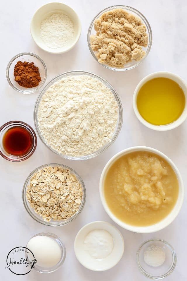 Ingredients for applesauce muffins in separate containers on a white background.