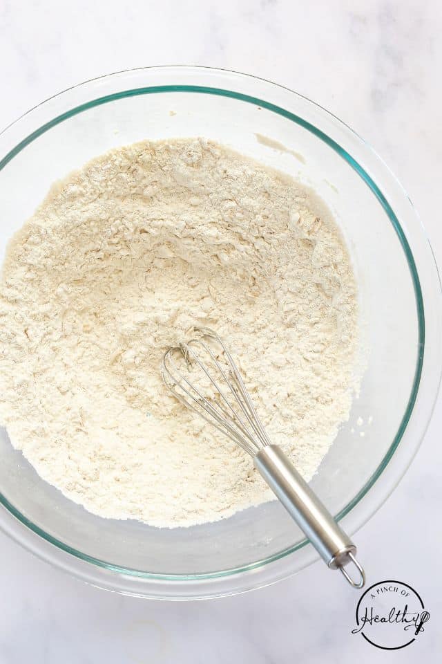 Dry ingredients for applesauce muffins in a large glass bowl with a whisk.