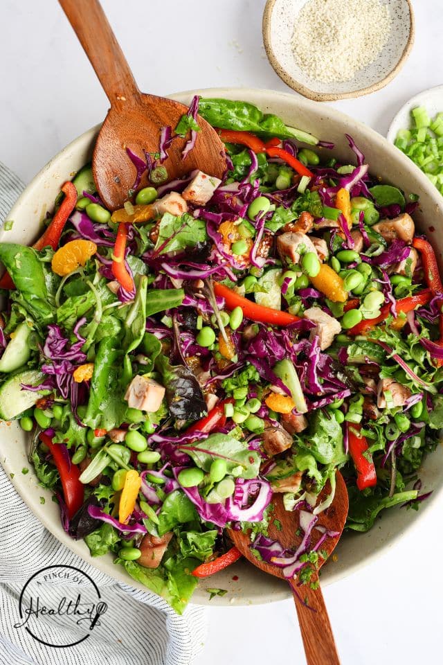 Asian chicken salad in a white bowl with a wooden spoon.