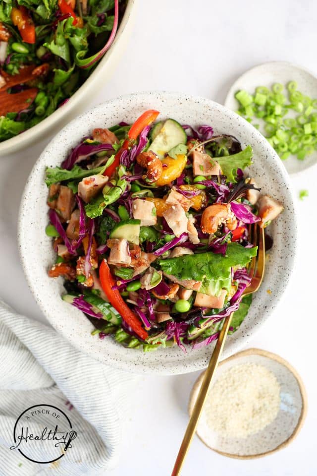 Asian Chicken Salad in a large white bowl with a gold spoon.