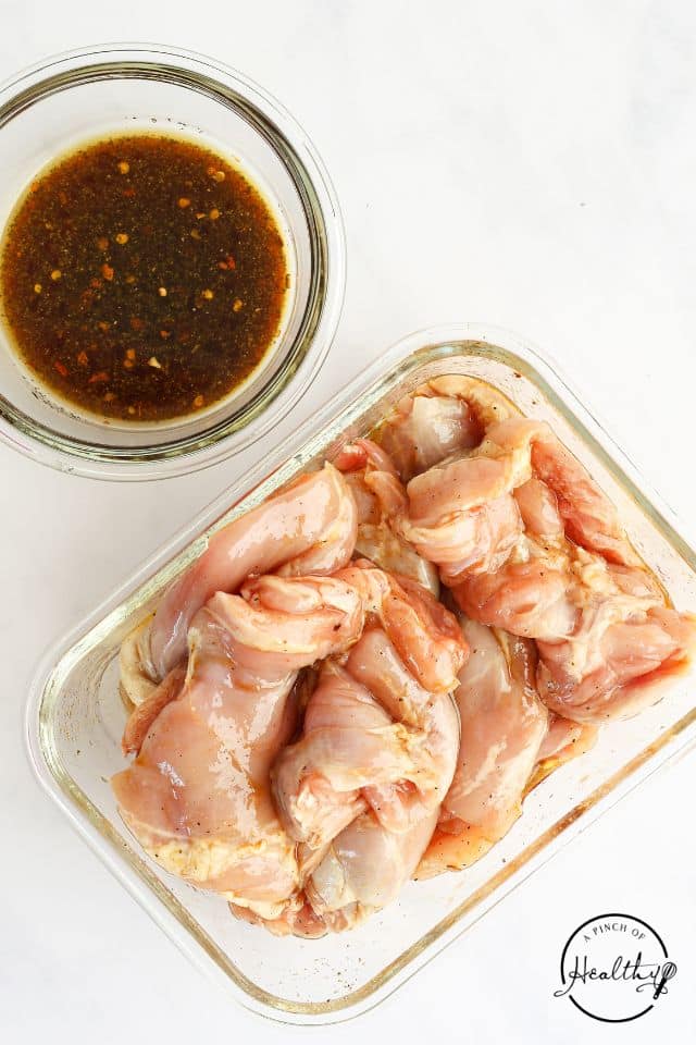Chicken in a large rectangular container next to a dish of the sauce.