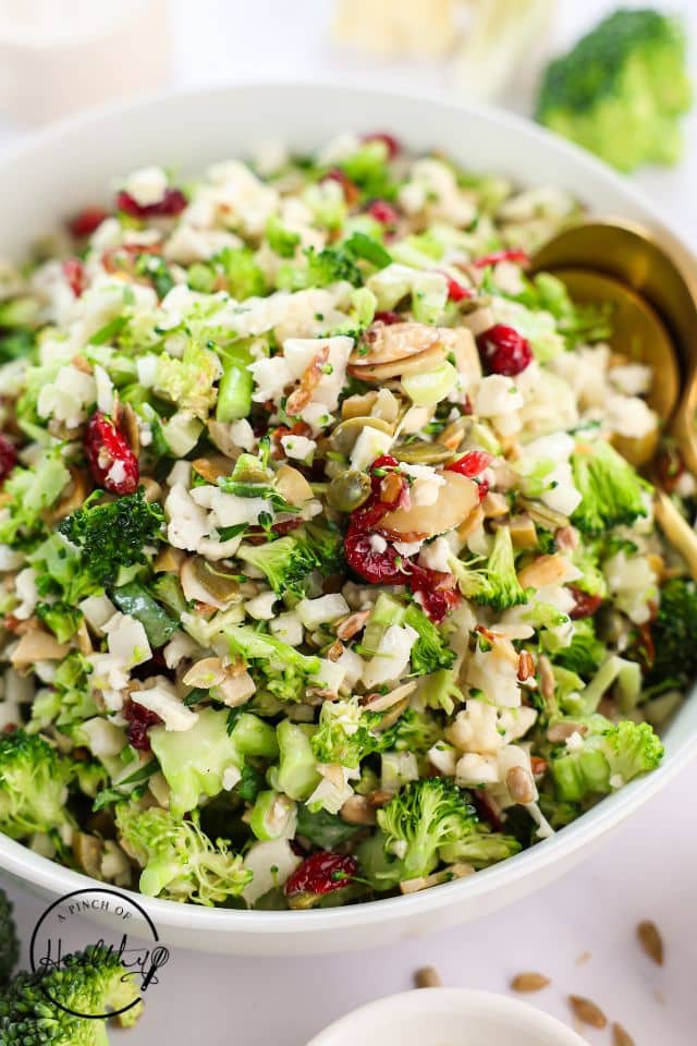 Broccoli cauliflower salad in a large bowl with gold serving spoons.