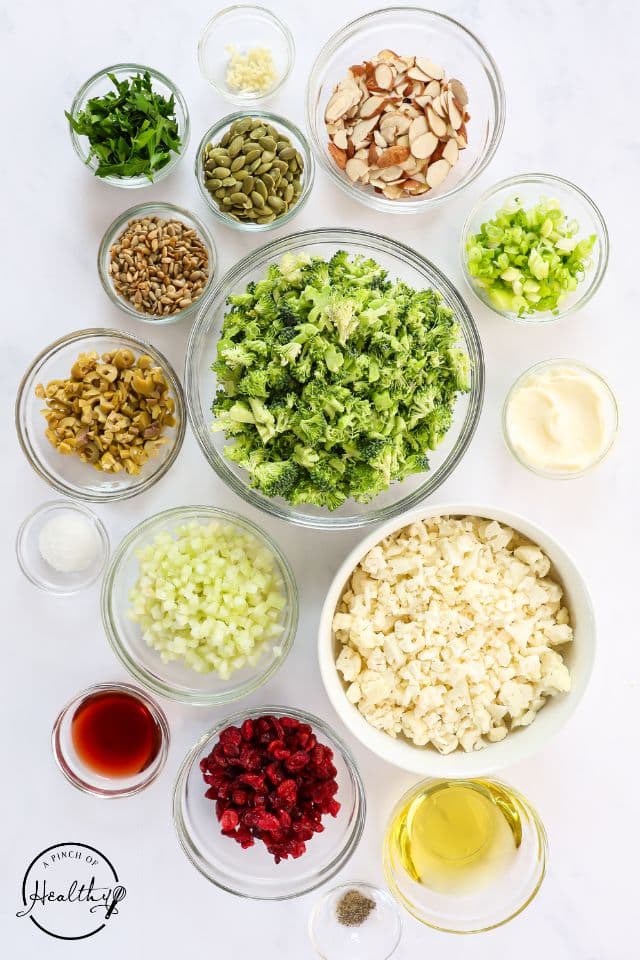 Ingredients for broccoli cauliflower salad in separate containers on a white background.