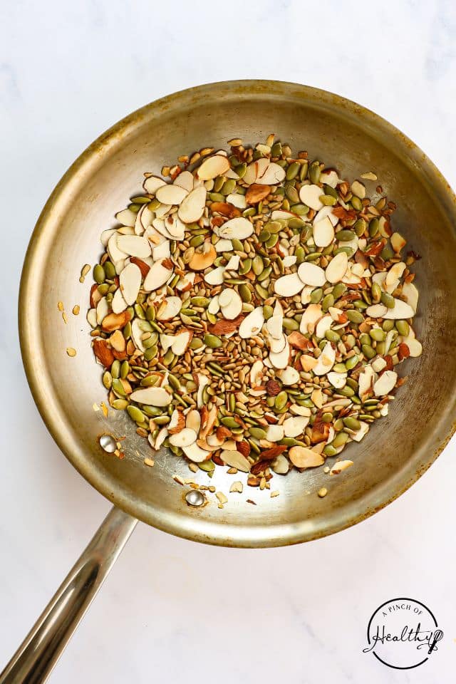 Seeds and nuts in a large skillet toasting on the stovetop for broccoli cauliflower salad.