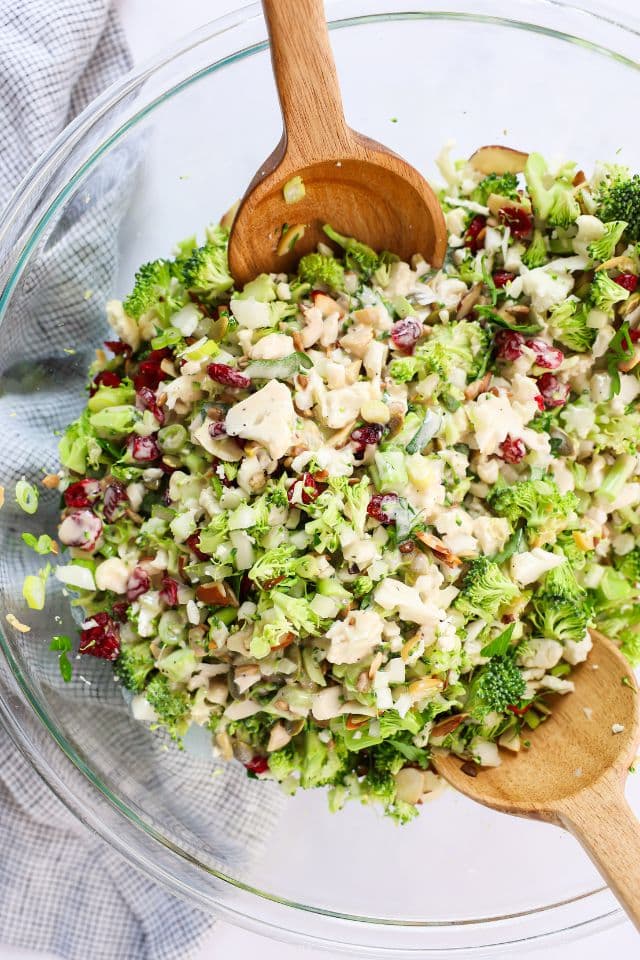 Mixing the dressing into the broccoli cauliflower salad with a large wooden spoon.