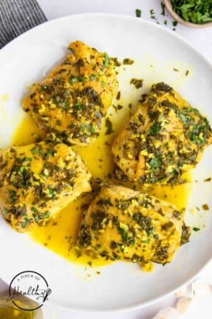 Crock pot chicken thighs on a white plate with sauce poured over the top.
