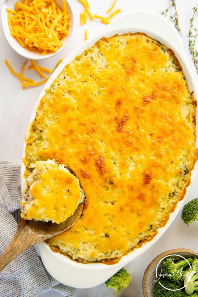 Broccoli cheese casserole in a large baking dish with a spoon removing a portion.