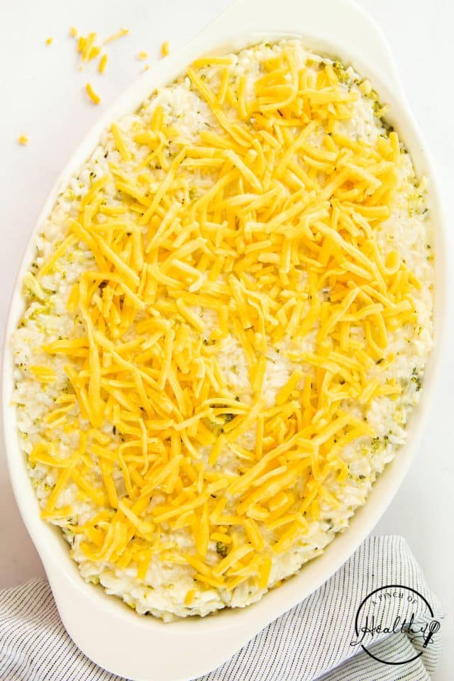 Mixture for broccoli rice casserole in a baking dish with shredded cheese on top before being baked.