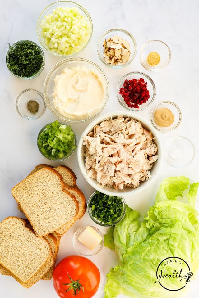 Ingredients for chicken salad sandwiches in separate containers on a white background.