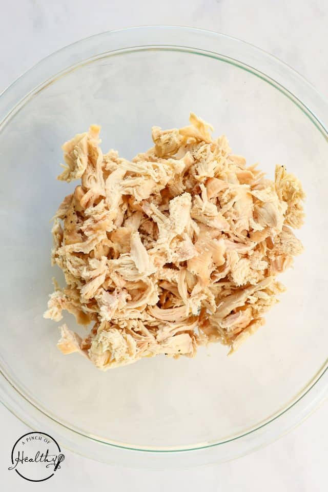 Cooked shredded chicken in a large glass bowl.