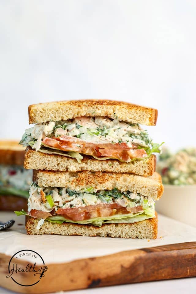 A chicken salad sandwich cut in half and stacked on top of each other on a cutting board.