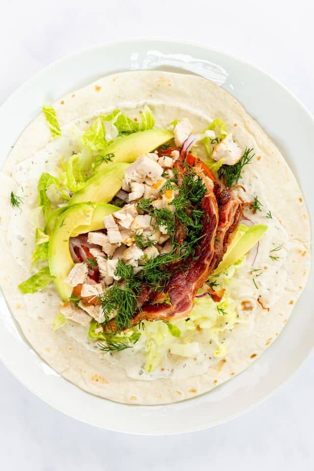 Chicken ranch wraps being assembled on a tortilla.